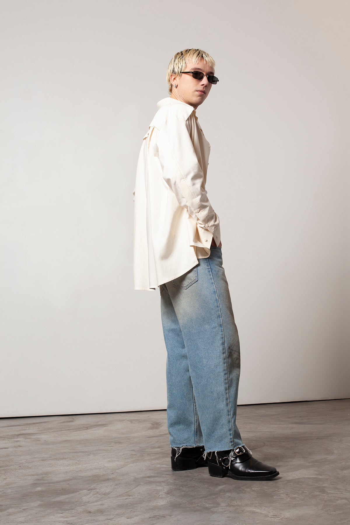 Clément is wearing White Canvas sustainable natural beige color, organic cotton oversized, genderless, inclusive, seasonless casual shirt, size L/XL styled with blue jeans and black sunglasses and shoes. The Essential shirt has minimal modern aesthetics design allowing comfort and bringing self-confidence. A limited-edition production is made locally in France to reduce environmental impact and guarantee high quality and durability of the products.
