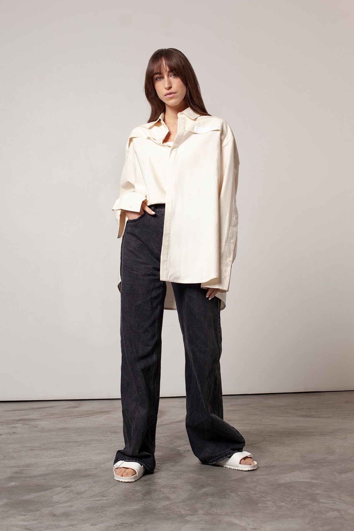 Léa is wearing White Canvas sustainable natural beige color, organic cotton oversized, genderless, inclusive, seasonless casual shirt, size S/M styled with black jeans. The Essential shirt has minimal modern aesthetics design allowing comfort and bringing self-confidence. A limited-edition production is made locally in France to reduce environmental impact and guarantee high quality and durability of the products.