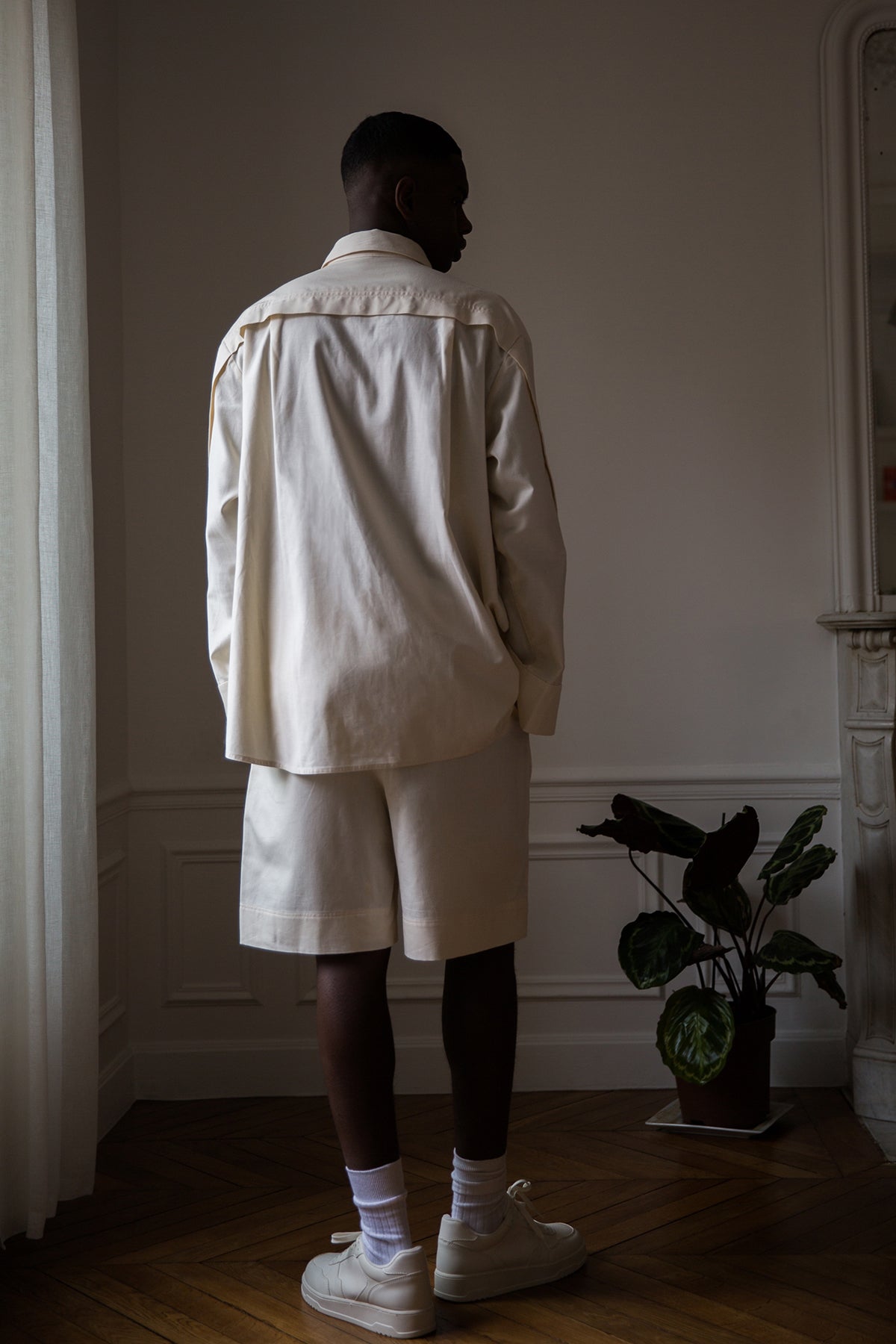 Thierno is wearing White Canvas sustainable natural beige color, organic cotton, genderless, inclusive, casual short, size M styled with a white tank top. The Essential short has minimal modern aesthetics design allowing comfort and bringing self-confidence. A limited-edition production is made locally in France to reduce environmental impact and guarantee high quality and durability of the products.