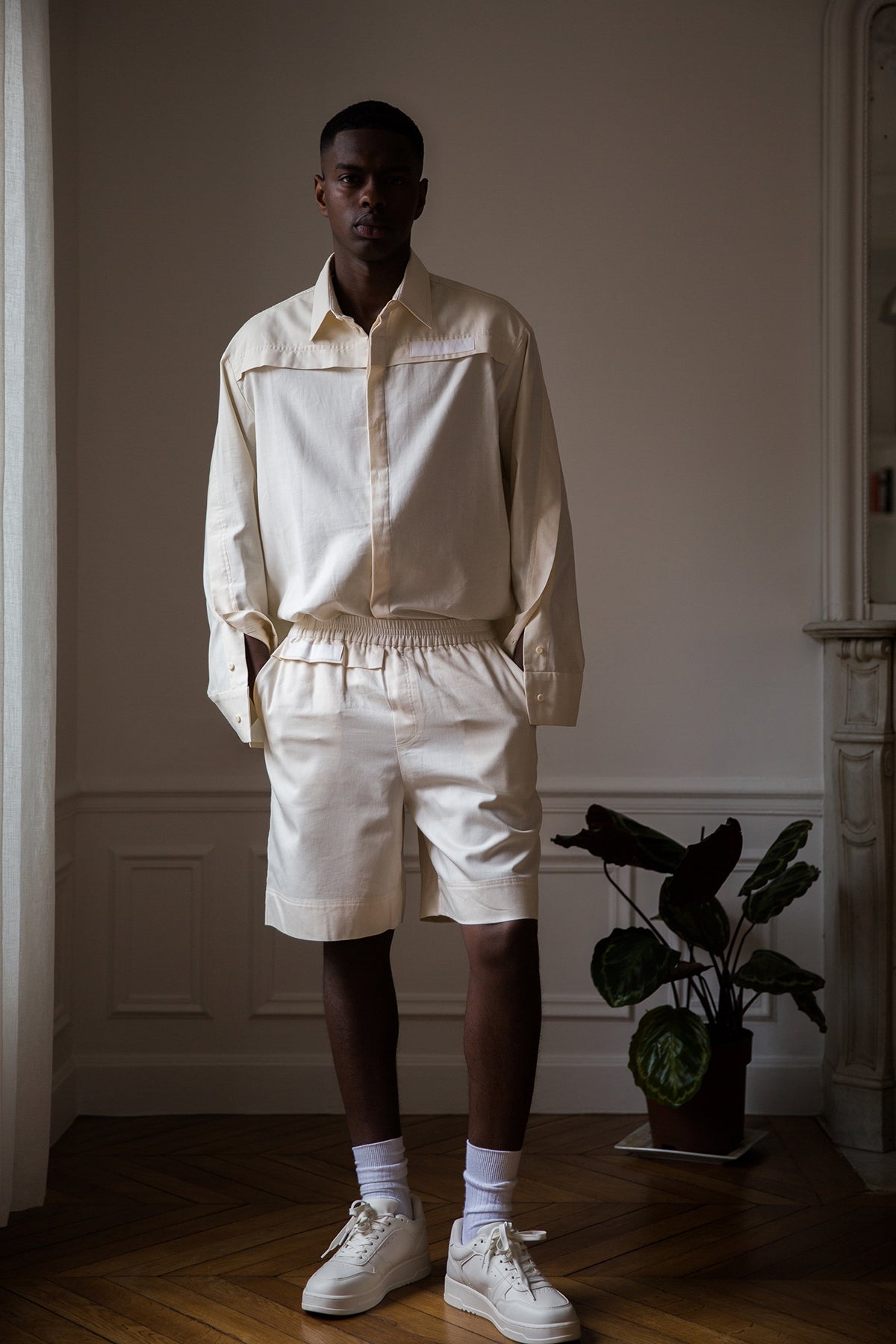 Thierno is wearing White Canvas sustainable natural beige color, organic cotton, genderless, inclusive, casual short, size M styled with a white tank top. The Essential short has minimal modern aesthetics design allowing comfort and bringing self-confidence. A limited-edition production is made locally in France to reduce environmental impact and guarantee high quality and durability of the products.