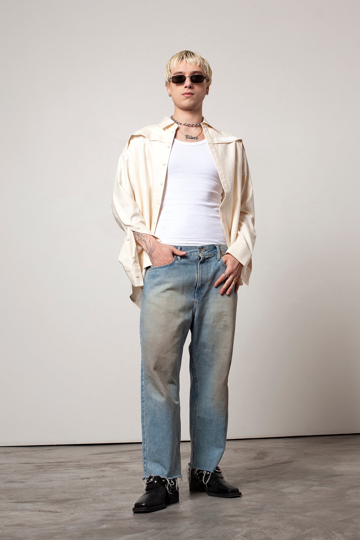 Clément is wearing White Canvas sustainable natural beige color, organic cotton oversized, genderless, inclusive, seasonless casual shirt, size L/XL styled with blue jeans and black sunglasses and shoes. The Essential shirt has minimal modern aesthetics design allowing comfort and bringing self-confidence. A limited-edition production is made locally in France to reduce environmental impact and guarantee high quality and durability of the products.