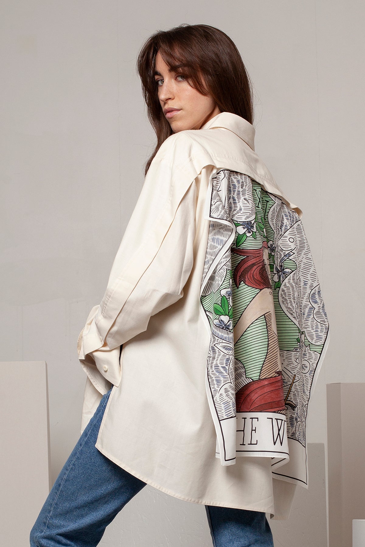 Léa is wearing the White Canvas ESSENTIAL SHIRT styled with THE WORLD foulard and square panel made from leftover deadstock silk fabric. The foulard has an exclusive design inspired by tarot cards drawn by the artist Maria Robla, printed with black artisanal eco-friendly ink locally in Paris and hand painted by the artist. Wear the foulard alone or attach it to the essential pieces to personalize them and wear them your unique way. Your perfect summer accessory. White Canvas x Maria Robla.