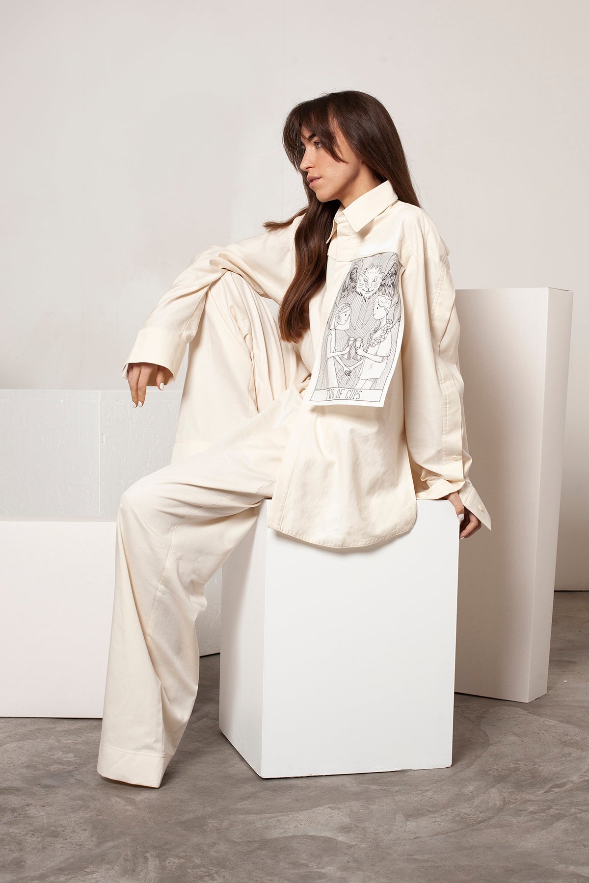 Léa is wearing the White Canvas ESSENTIAL SHIRT styled with THE TWO OF CUPS vertical panel made from leftover deadstock white cotton poplin. The panel has an exclusive design inspired by tarot cards drawn by the artist Maria Robla and printed with black artisanal eco-friendly ink locally in Paris in collaboration with RoStudio. Attach the black and white panel to the essential pieces to personalize them and wear them your unique way. Your perfect summer accessory.
