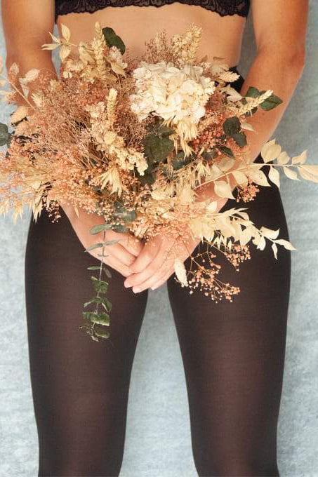 Jeune femme de face arborant un bouquet de fleurs séchées porte un collant noir opaque en graines de ricin.