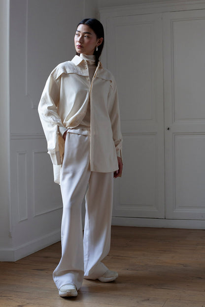 SiJia is wearing White Canvas sustainable natural beige color, organic cotton oversized, genderless, inclusive, seasonless casual shirt, size S/M styled with wool trousers. The Essential shirt has minimal modern aesthetics design allowing comfort and bringing self-confidence. A limited-edition production is made locally in France to reduce environmental impact and guarantee high quality and durability of the products. 