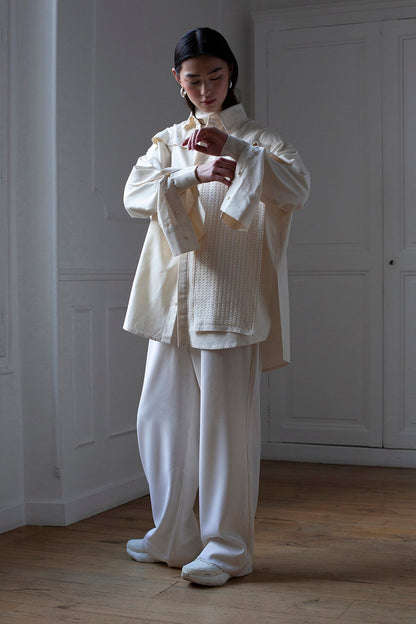 SiJia is wearing White Canvas sustainable natural beige color, organic cotton oversized, genderless, inclusive, seasonless casual shirt, size S/M styled with wool trousers. The Essential shirt has minimal modern aesthetics design allowing comfort and bringing self-confidence. A limited-edition production is made locally in France to reduce environmental impact and guarantee high quality and durability of the products. 