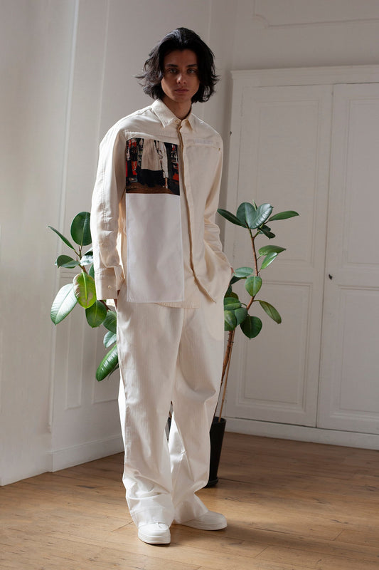 Medhi is wearing the White Canvas essential shirt styled with the Trench Coat vertical panel made from deadstock cotton poplin. The panel has an exclusive print of a photo by the photographer Henrique Soares. Attach the panel to the essential pieces to personalize them and wear them your unique way. It is the perfect creative autumn accessory.